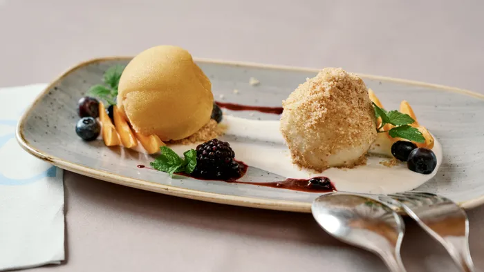Gourmet-Dessert mit Mangosorbet, Bröselknödel, Beeren und Obst auf Sahnesauce